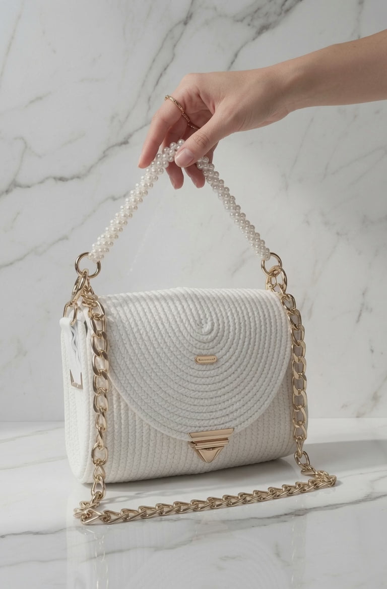 Bolso Clutch Blanco artesanal Media Luna con cadena dorada extraíle y asa de perla. La mano gira suavemente un bolso enseñandole sus detalles.